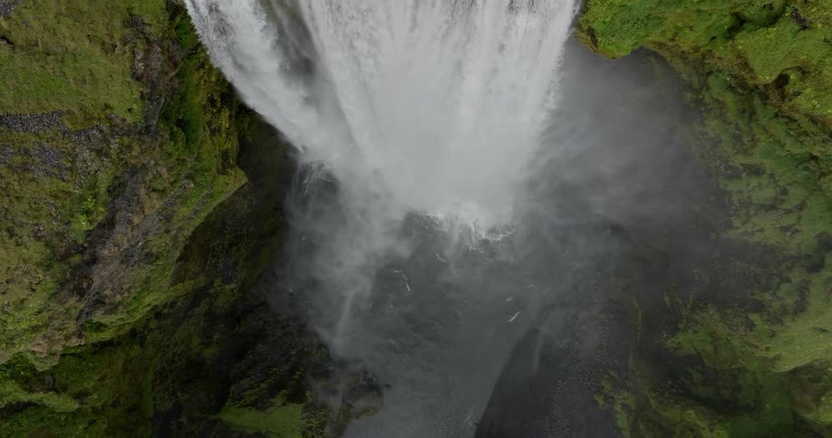A waterfall crashes into a river between moss covered mountains and cliffs