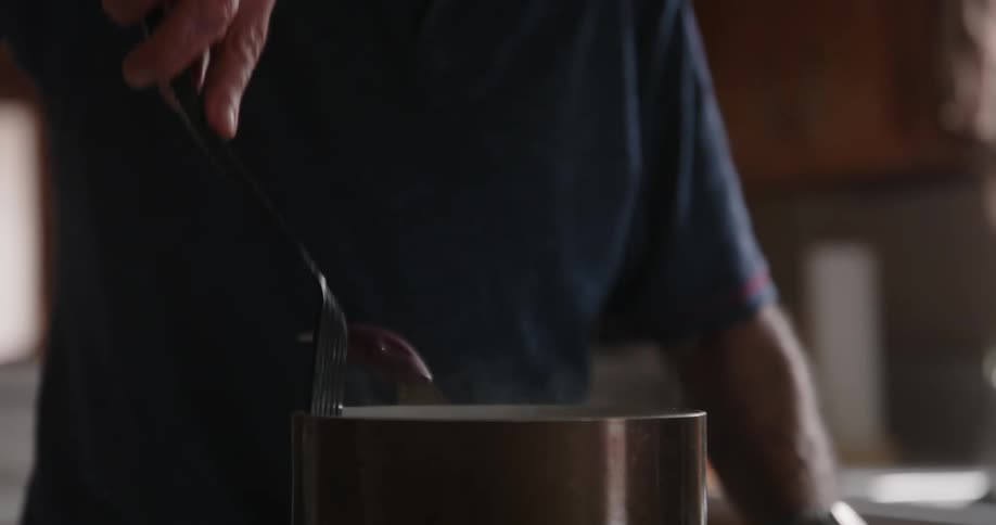 A man uses utensils to mix the food he is cooking in a steaming pot