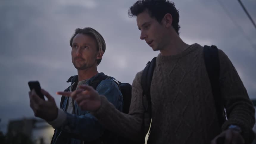Two traveling men walking at sunset while checking their mobile phone