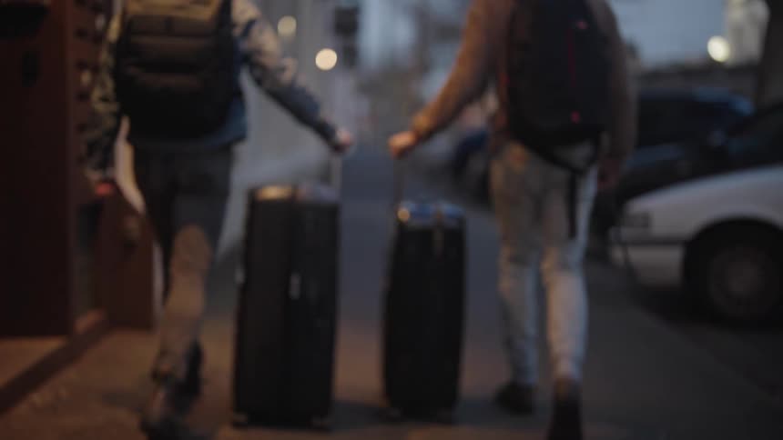Two men walking on the sidewalk with traveling boxes at night