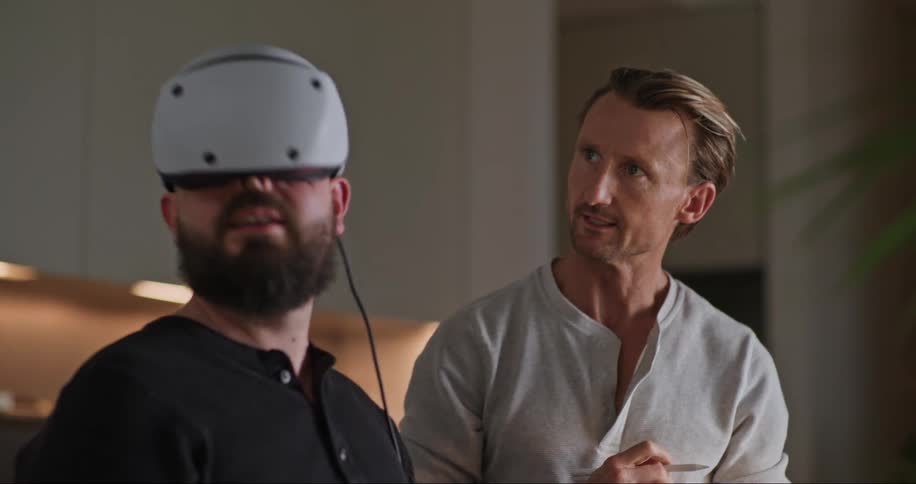 Two men in an indoor setting one wearing virtual reality glasses and the other holding a tablet and a pen