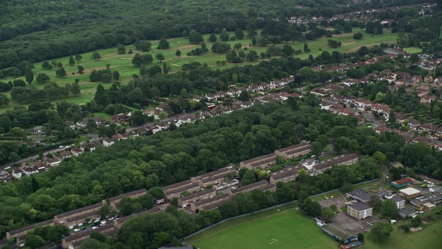 Traffic moves on the roads of suburban neighborhoods with trees and fields and a forest in the distance