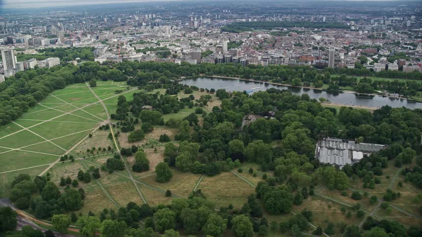 A park with green vegetation and grass and a lake is in the middle of a city