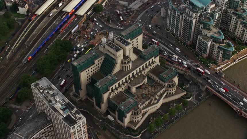 Vehicles on train tracks and streets move past blue accented architecturally detailed building