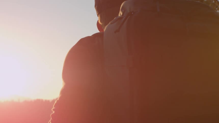 A man is wearing a backpack as the sun sets