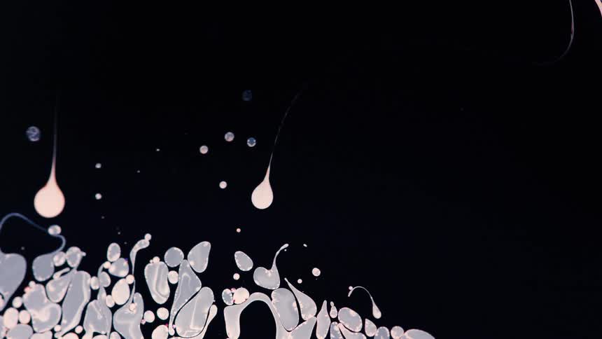 Drops of white ink float over a dark backgroundtion