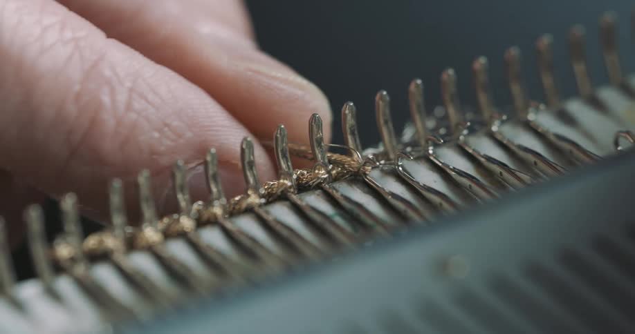 A adult worker is placing gold thread into a metal clasp