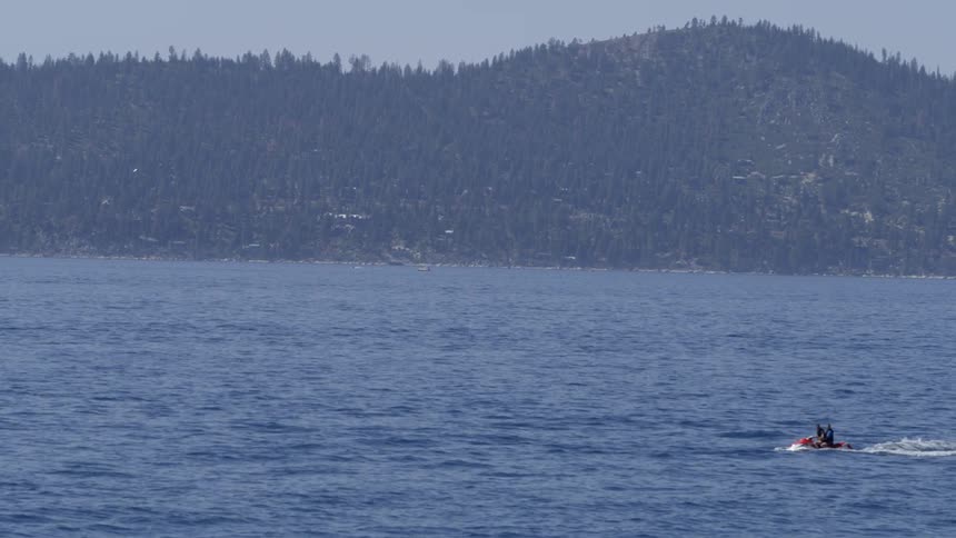 Two people are riding in the water ahead on a jet ski