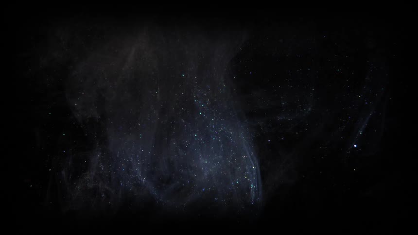 A cloud of shimmering particles float in a cloud over a dark background