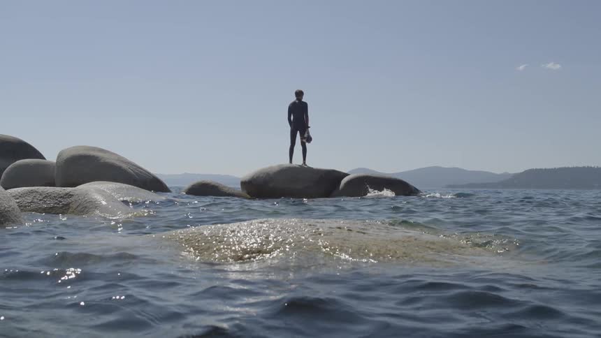 A man is standing on a rock in the water on a sunny day
