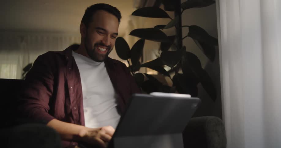 Happy man sits on a couch to work on a computer