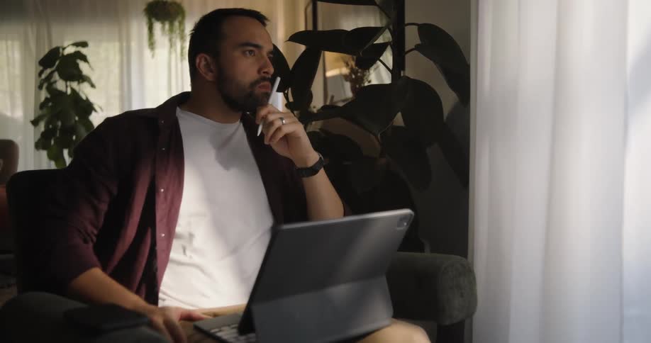 Man sitting in an armchair looking thoughtful with his tablet