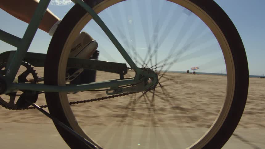 A bicycle rider rides on a path at a sandy beach