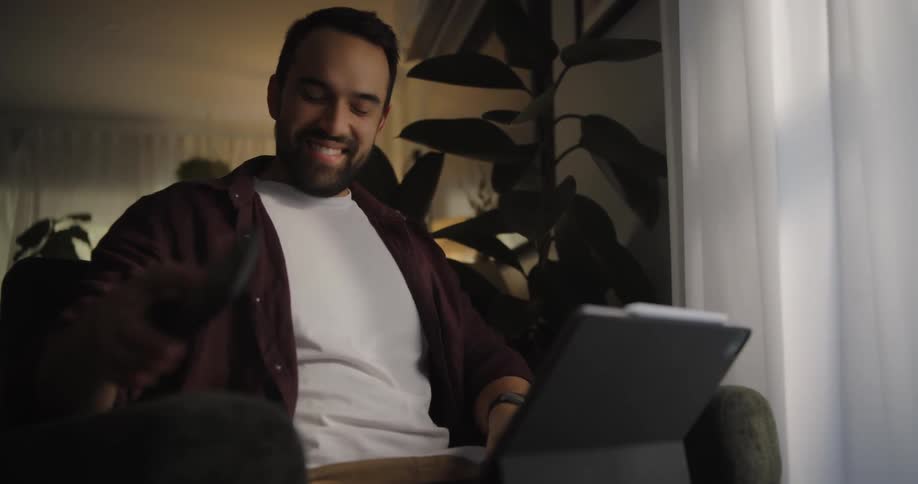 Man sitting in an armchair using his laptop smiling in an indoor environment