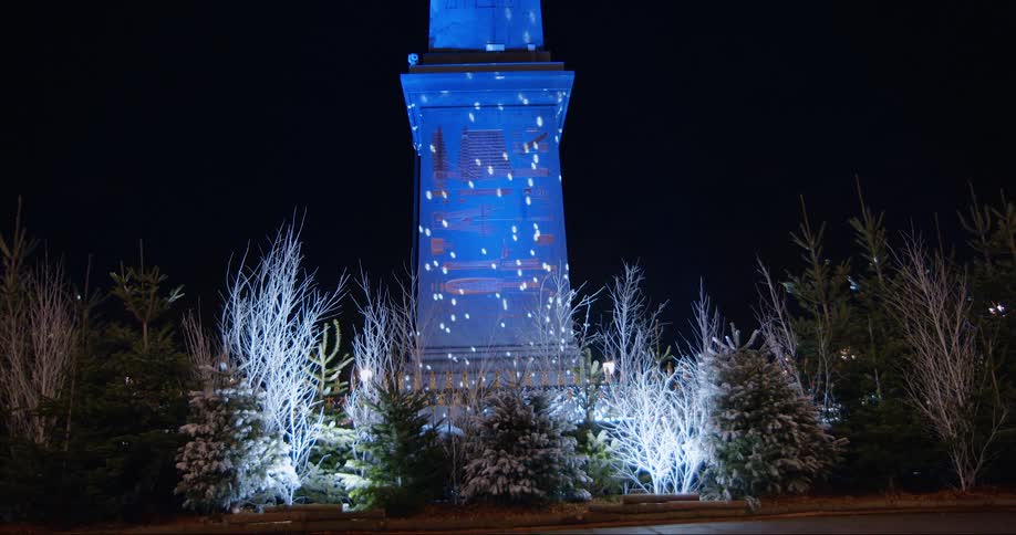Blue light and colorful dots of light shining over a monument surrounded by bushes and trees at night time