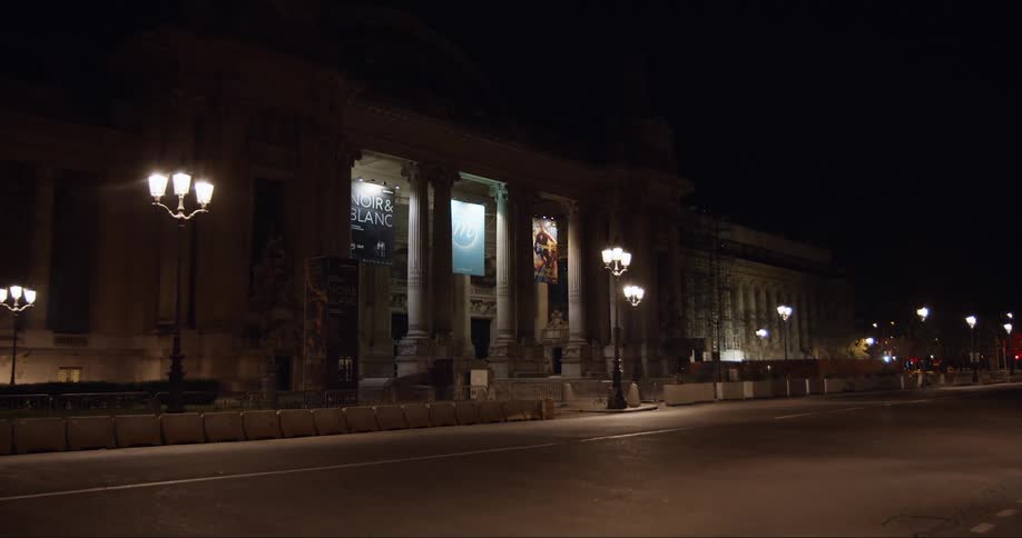 The facade of a litup city museum building can be seen from the road at night