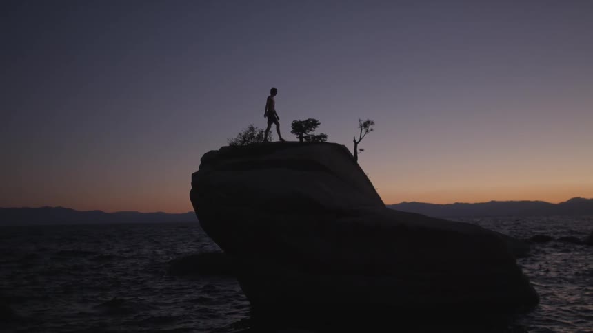 A man is walking on the edge of a cliff at dawn