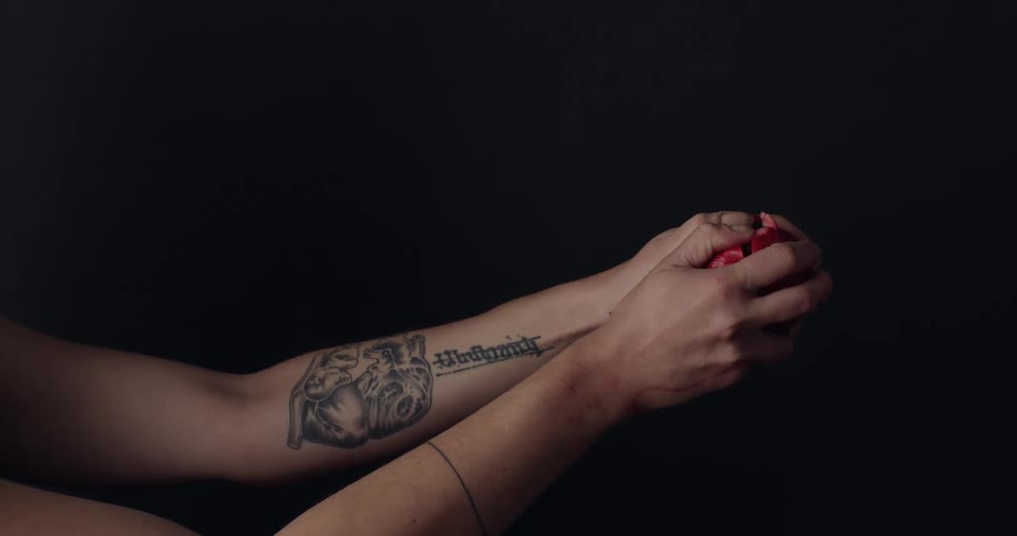 A womans hands squeezing a red fruit against a black background