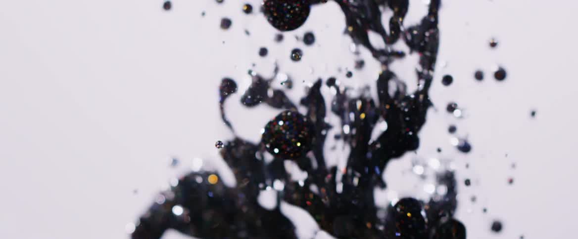 A black glittery liquid flows into a translucent fluid