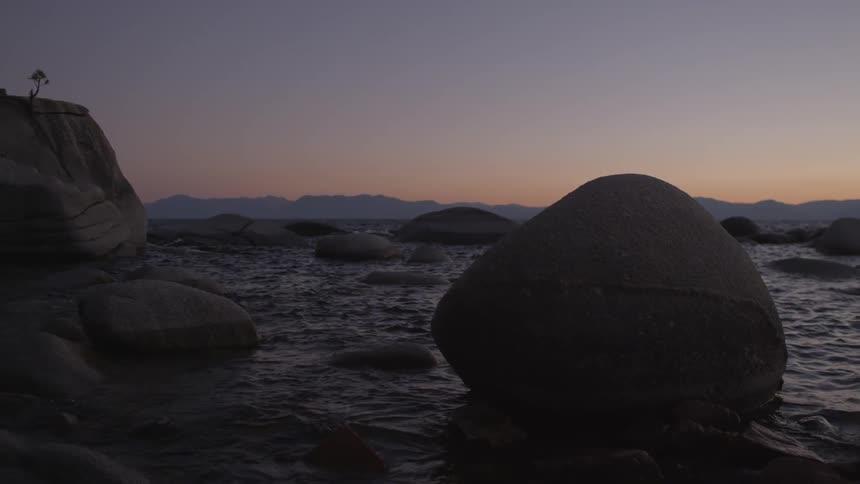 Large rocks are surrounded by rough waters at sunset
