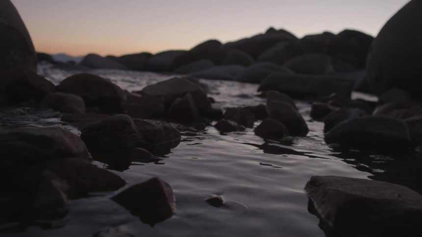 The shore is lined with rocks at sunset