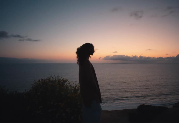 Silhouette of a young woman standing next to the ocean at sunset