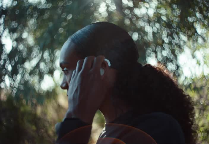 Woman standing outdoors puts on hearing aids