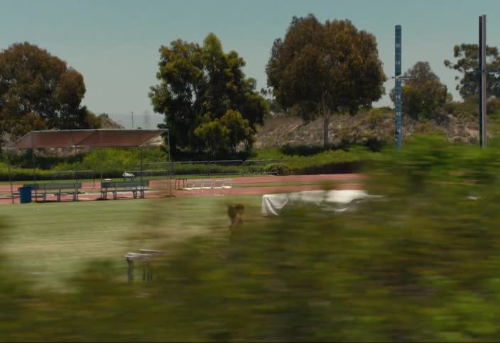 A woman athlete running outdoors next to a track on a field in the middle of a sunny day