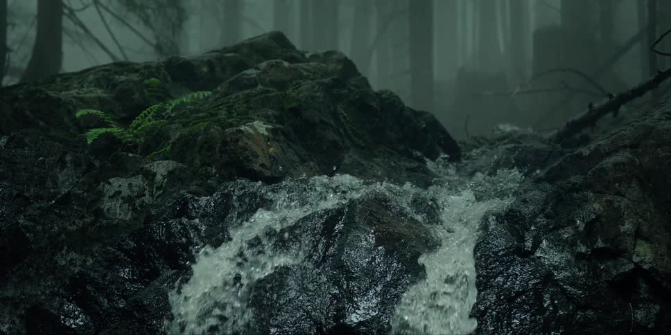A waterfall cascades over mossy rocks in a dark forest