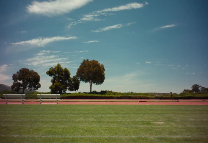 A person running on an outdoor track near trees and grass on a bright sunny day