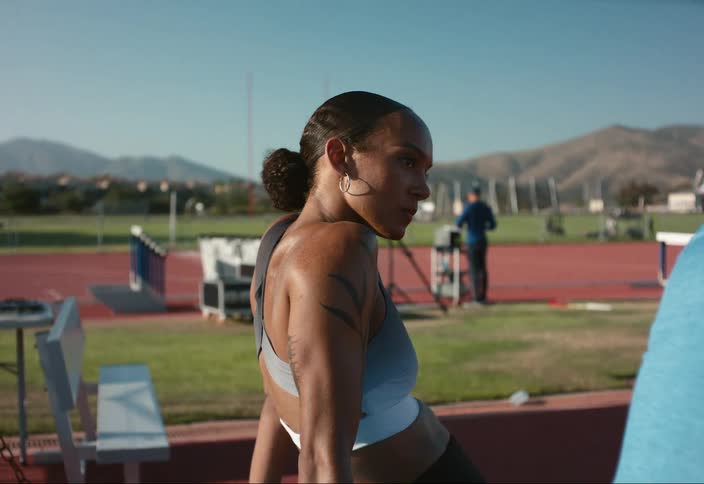 A female conversing with another person on a track field at midday