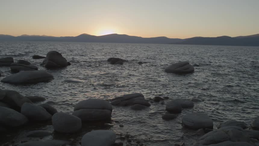 The water splashes against the rocks at sunset