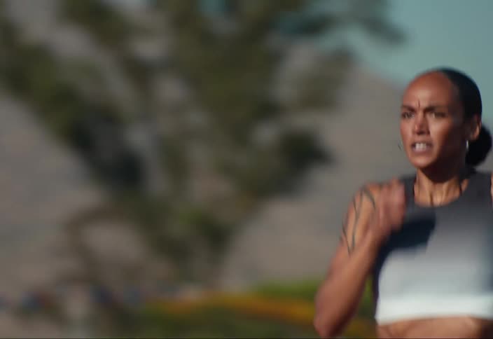 A young woman running outdoors at a track meet in the sun