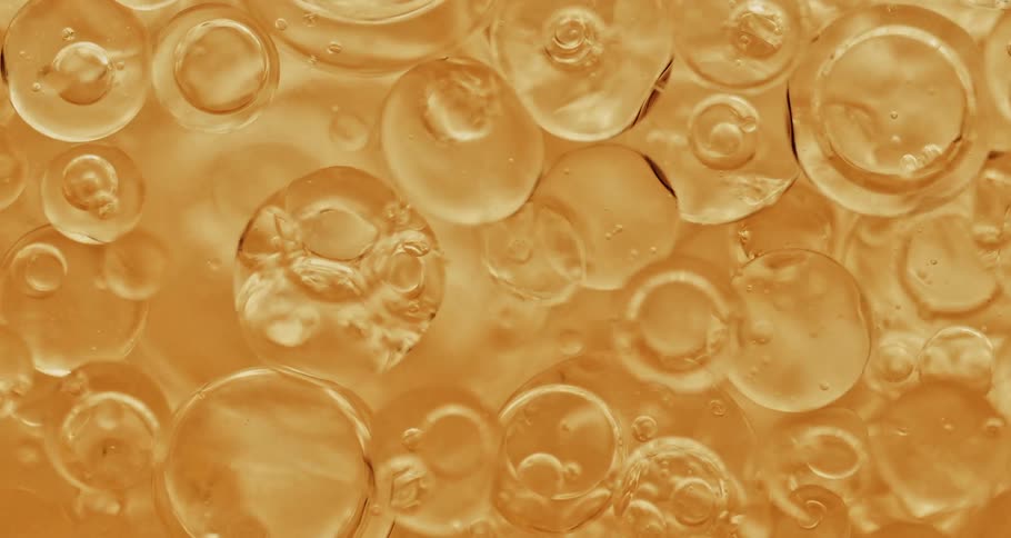 Transparent bubbles cluster together while floating over peach fluid