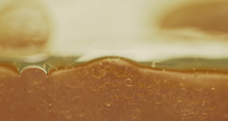 Orange oily bubbles slowly settling into liquid against a glass