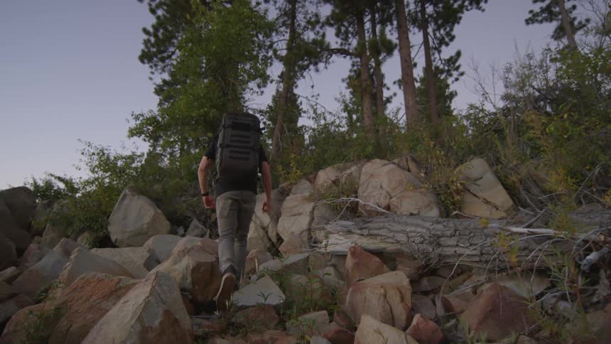A man is climbing up rocks at sunset