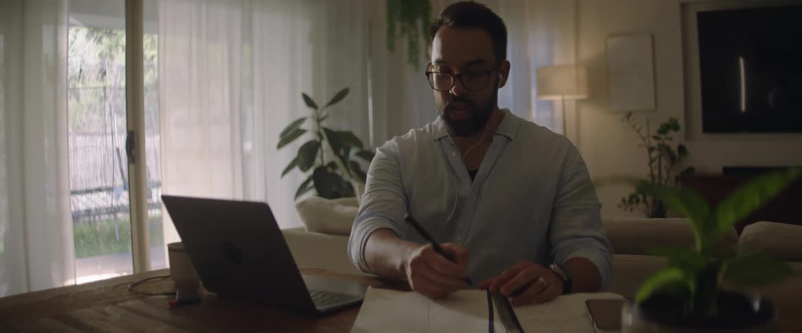 A man is writing notes while looking at his laptop