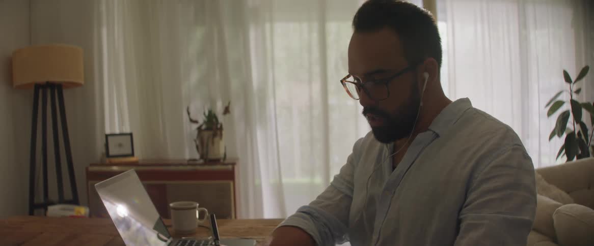 A man is taking notes while looking at his laptop
