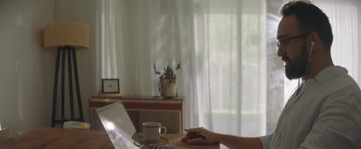 A seated man is drinking something and shortly after waving and chatting with agluem through a laptop