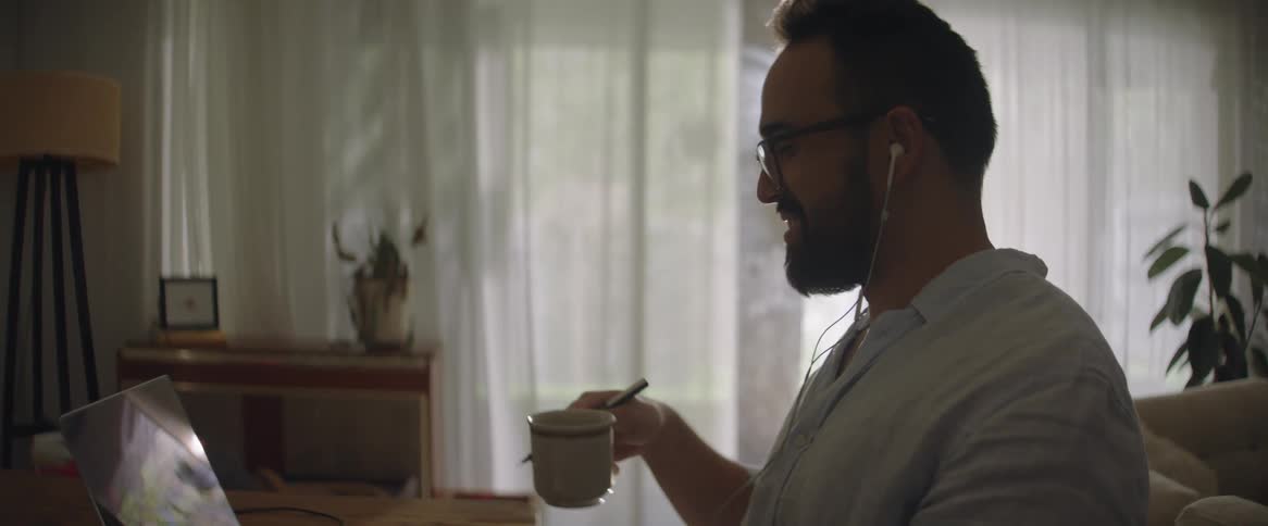 Man drinks coffee and laughs during video call at home