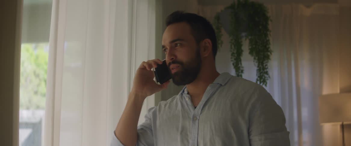 Man standing near glass doors in home smiles while talking on phone