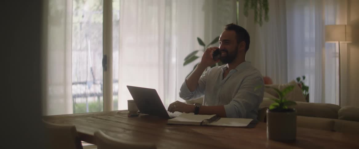 A man is talking on his cell phone while typing on his computer