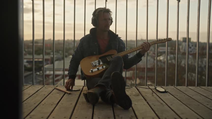 A man sitting playing his guitar and picking up a notepad