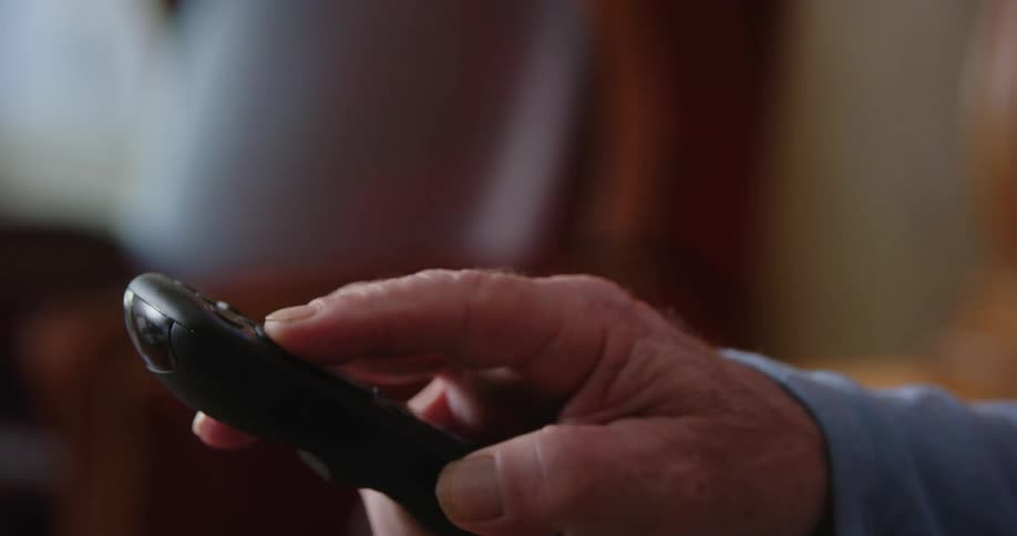 An elderly man operates a television remote control