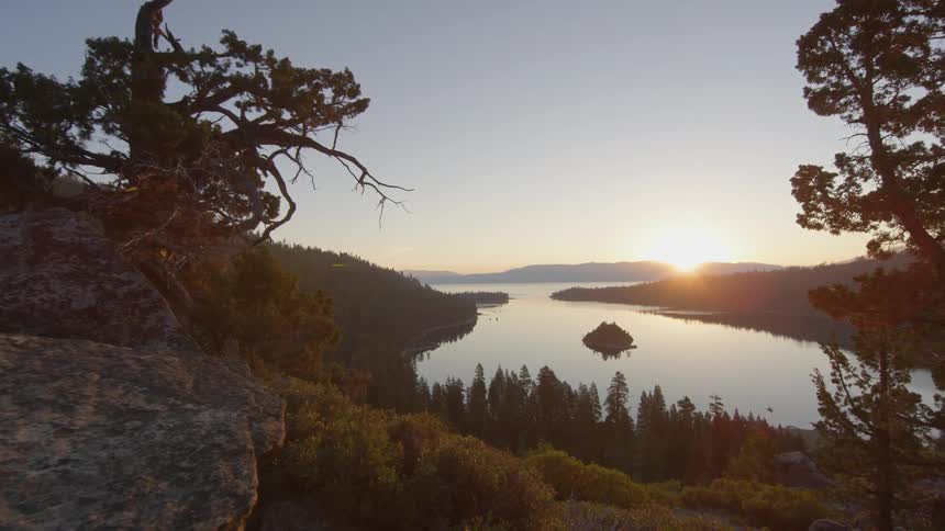 Down the hill is a lake with a sun setting in the distance