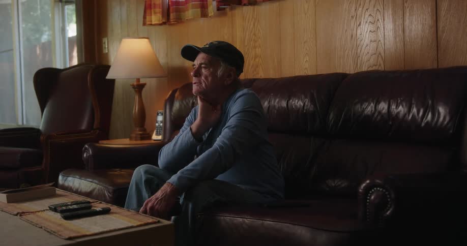 An elderly man celebrate while sitting on a couch indoor at midday