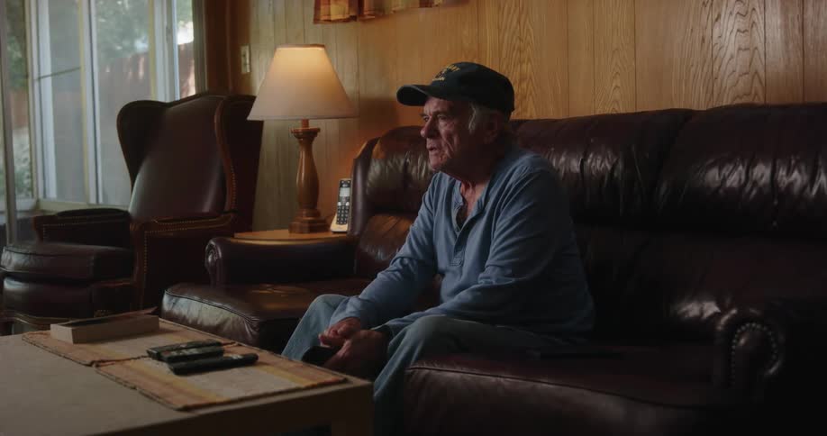 An elderly man commenting while sitting on a couch indoor