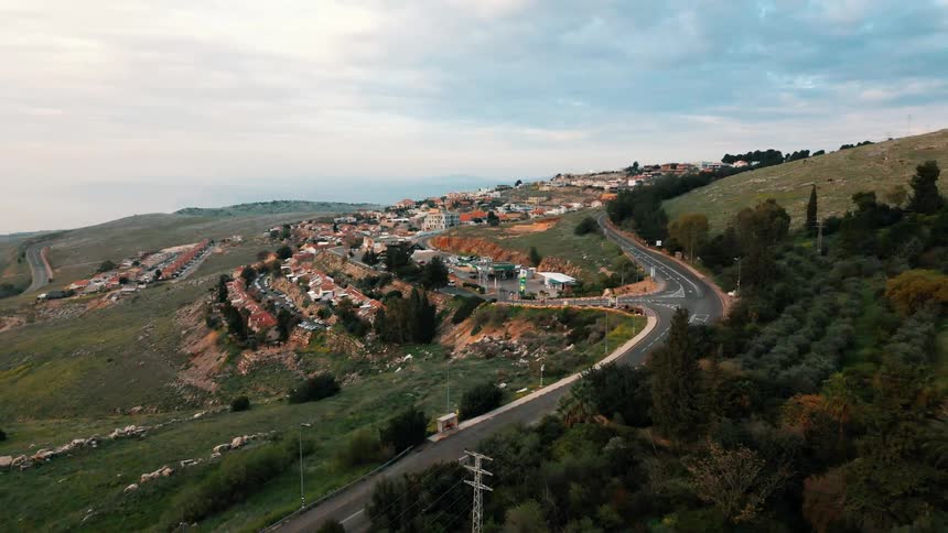 Drone view of a roadway traveling along a hillside toward a suburban neighborhood on a bright sunny day