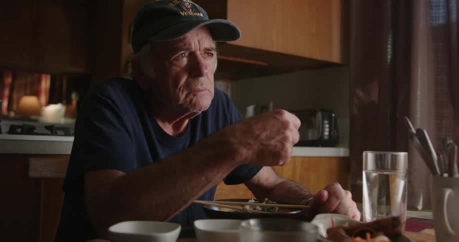 An elderly man looking stressed while eating in the kitchen