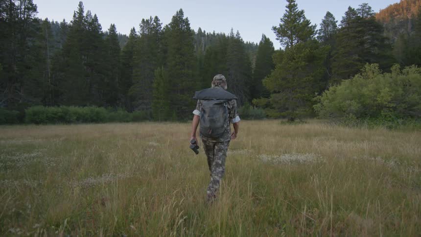 A man is hiking along the grass on a sunny day